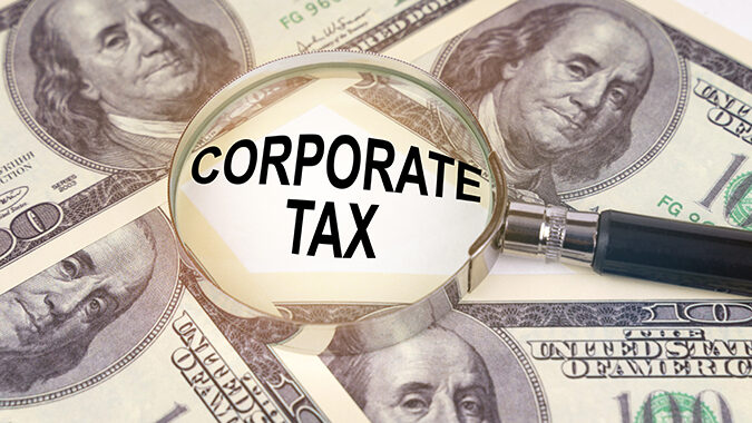 Among the dollars lies a magnifying glass with the inscription - Corporate Tax