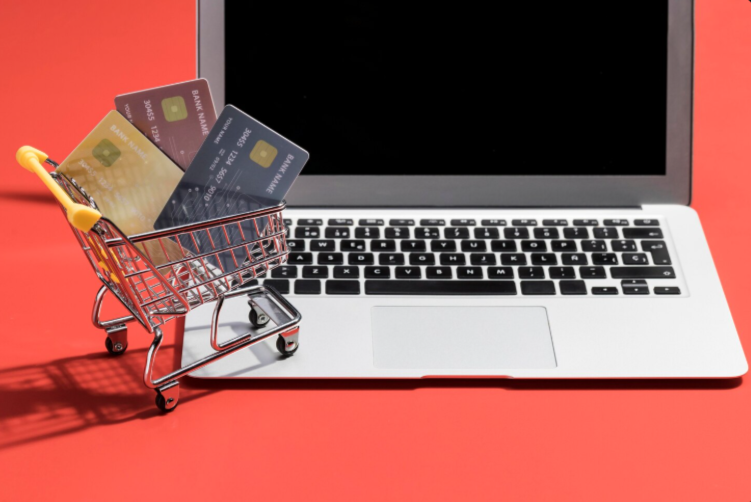 Credit cards in a tiny shopping cart near a laptop.